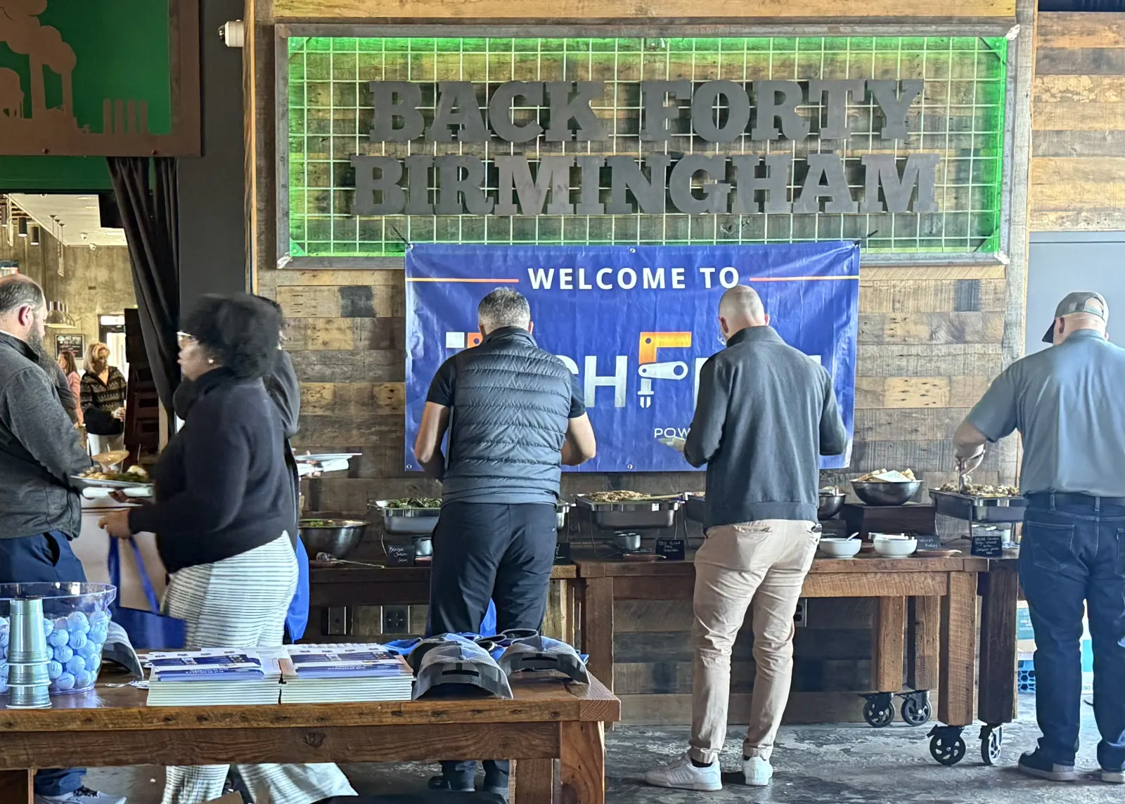 Attendees at the food line under the Back Forty Birmingham and TechFest welcome banner